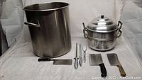 Full view of kitchen lot showing large stainless steel stock pot, stainless steel steamer pot, three cleaver knives, Gerber USA carving knife and fork, and sharpener