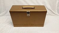 Closed metal file box showing rectangular shape, brownish color, handle on top and front latch.