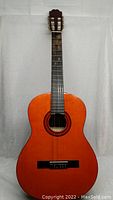 Front view of the orange-toned Suzuki classical guitar showing the sound hole, rosette, and worn fretboard.