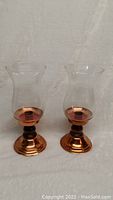 Pair of vintage copper hurricane lamps with clear glass chimneys, placed side by side on a white background.