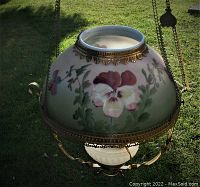 Full view of lamp outdoors showing painted floral shade, brass fittings and milk glass font