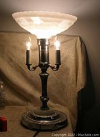 Front angled view of torchiere lamp illuminated showing frosted etched glass bowl and three bulb holders with bulbs lit.