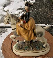Porcelain figurine of a lady equestrian riding a white Lippizaner horse on a decorated base, viewed from the front with floral base details visible.