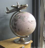 Front view of the chrome metal revolving globe with the airplane figure mounted on top, showing the globe's aged vintage-style map design and chrome base.
