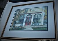 Framed art print showing a colorful depiction of the Niagara Apothecary storefront with a bicycle and autumn trees.