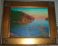 Frontal view of the painting showing natives in canoe, dock, cabin, and wooded landscape with gilt frame.