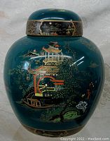 View of the front and left side of the Carlton Ware porcelain lidded jar showing detailed chinoiserie scene with pagodas and trees on deep teal background.