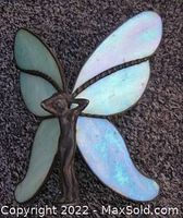 Winged fairy statue lying on carpet showing front with iridescent light blue and pink stained glass wings and dark metal figure.