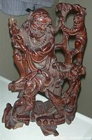 Front angle view of large antique carved rosewood Chinese figural sculpture showing seated male figure, children, and bird with some missing chips on base and staff.
