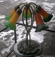 Front view of the five lily-shaped art glass shades and metal base showing the color gradient and lily leaf motif on base.