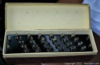 Top view of the open box showing the capo chordmaker with chrome metal levers and tuning pegs on a black base.