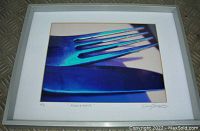 Framed photo of a blue-toned fork and knife close-up with white mat and signature, silver frame, laying flat on a surface.