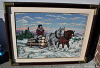 Frontal photo of vintage wood framed needlepoint artwork showing a winter sleigh scene