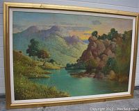 Full frontal view of framed landscape painting showing river, rocky hillside, mountains and sunset sky
