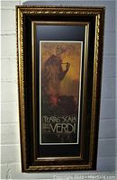 Frontal view of the vertical Verdi poster in ornate gold wood frame with black matte border against a brick wall.
