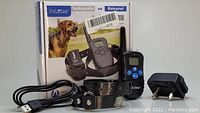 Full lot contents showing training collar, remote, USB cable, power adapter, and box with product branding and image of a dog.