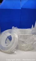 Five rolls of clear tape individually wrapped in plastic on white surface with blue backdrop