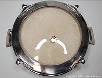 Top view of an antique pie plate with beige ceramic center and stainless steel carrying dish with handles.