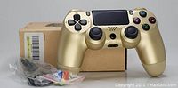 Metallic gold PS4 controller with original box, cables and extra thumb grips visible.