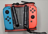 Photo of Nintendo Switch Classic Joy-Con controllers in blue (left) and red (right) with control straps attached. Controllers are resting on a box with a diagram.