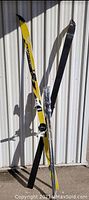 Pair of yellow Rossignol skis and Gipron poles standing against a white metal wall.