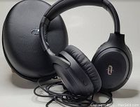 Black wireless over-ear headphones positioned in front of a black hard carrying case, with charging cord placed in front.
