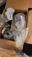 Box containing multiple new clear glass bottles with spray lids wrapped in plastic.