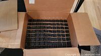 Top view of a cardboard box containing 80 blue glass bottles arranged in rows and separated by cardboard dividers.