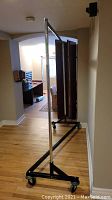 Photo showing full height metal clothing rack with chrome poles and black base frame on caster wheels.