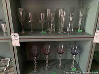 Top shelf containing six clear champagne flutes, wine glasses and a small carafe with various shapes and sizes.