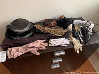 Overview of gloves, belts, scarf, vintage hats, hair dryer, mirror with crack, and hair brush laid out on drawer surface