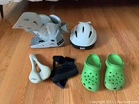 White SP Walker Aircast medium helmet, green Crocs, two white small braces, black strap, showing all items lay flat on wood floor