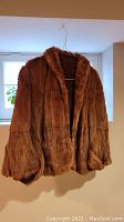 Front view of the brown mink fur crop jacket hanging on a hanger, showing the length, sleeves, and fur texture.