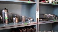 Wide view of silver plate coffee set items on shelf, including coffee pot, sugar jars, milk jar, decorative plate, glass bowl, and crystal ornaments