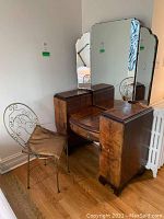 Vintage wooden vanity table with tri-fold mirror and drawers; shows surface damage and some drawers hard to pull out, placed against wall on hardwood floor.