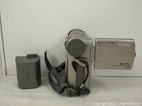 Front view of the silver Canon Elura 2 digital camcorder with lens cap on and included battery pack to the left.