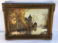 Framed artwork showing a church by the water with autumn trees and two people in a boat