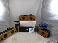 Setup of six speakers and one black Jam speaker pouch on white backdrop, showing various jazz-marley wooden bamboo design speakers and blue circular speakers with X and O symbols.