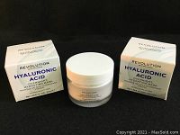 Photo showing the unopened white jars with white lids alongside their original boxes labeled with product and brand information.