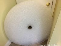 Top view of large, tightly wound roll of clear bubble wrap with circular cardboard core in center.
