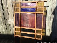 Front view of stained glass art window or door showing mostly purple and amber yellow panels with central large red panel in natural light outdoors.