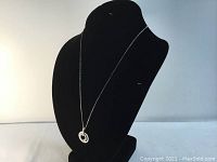 Full view of necklace on display bust showing openwork circular pendant with embedded clear crystals on silver rhodium plated chain.