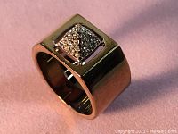 Close-up image of rose gold plated ring on pink background showing square face with clear crystals arranged in pattern.