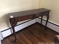 Full view of wooden sofa table against wall, showing two drawers and curved legs.