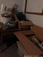 Overview of the lot showing boxes and bags on a wooden table against a white brick wall, containing Christmas decorations including wreath, garland and wrapping paper.