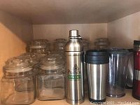 Shelf showing ten square clear glass containers with matching lids and three travel-size metal and plastic drink containers (two stainless steel, one plastic)