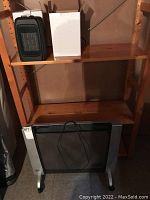 DeLonghi radiator on floor with power cord visible, showing overall size and design with black mesh and caster wheels