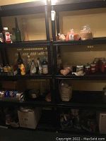 Three assembled black plastic shelving units against wall, stocked with household items