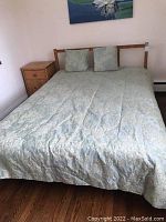 Assembled bed with coverlet and two pillows against wall