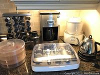 Overview of kitchen appliances on countertop including Delonghi coffee maker, Cuisinart ice cream maker, spice rack, electric kettle, and KitchenAid tool set case.